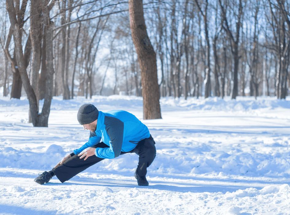 Muž před během venku na sněhu strečuje nohy-cz-alt