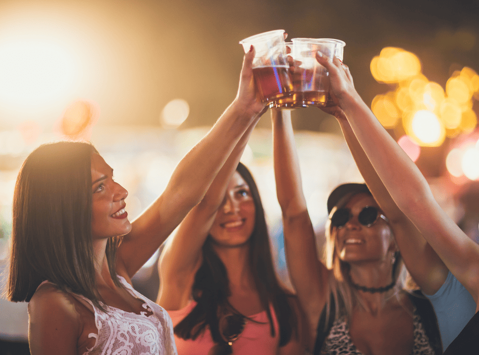 Tři mladé ženy si připíjejí pivem na letním festivalu v noci