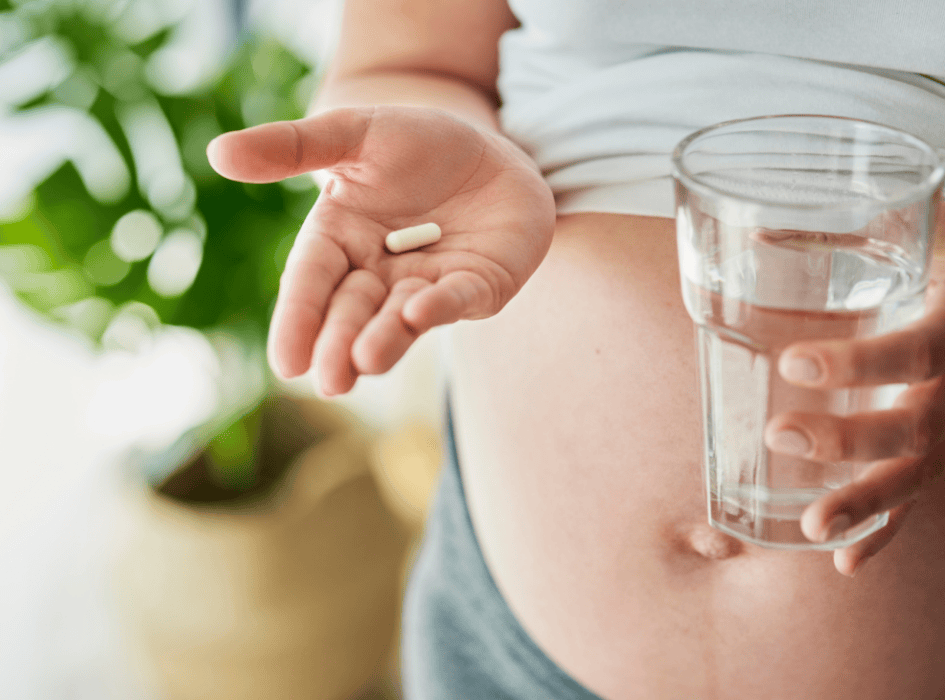 těhotná s břichem si dává vitamín a má sklenici vody