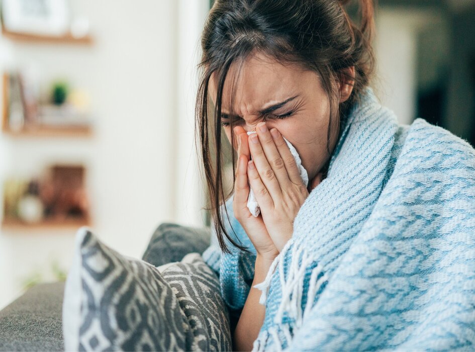 žena nemocná zabalená v dece smrká do kapesníku